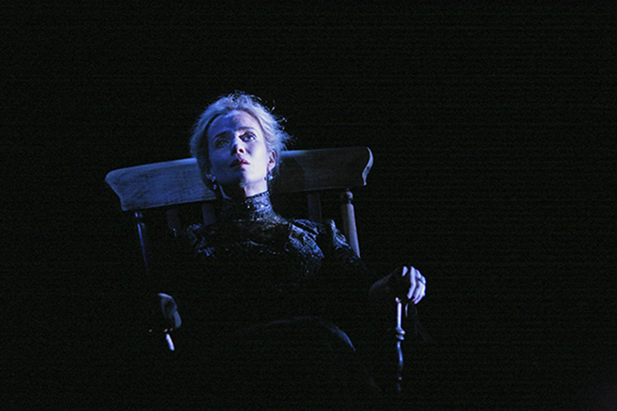 Lisa Dawns sits in a rocking chair on a dark stage
