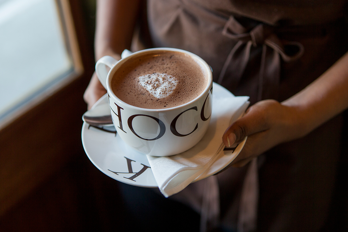 A person wearing a brown apron is holding a mug of hot chocolate.