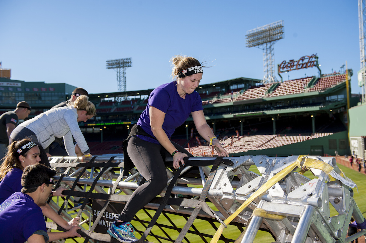 A woman climbs over a structure at Fenway Park