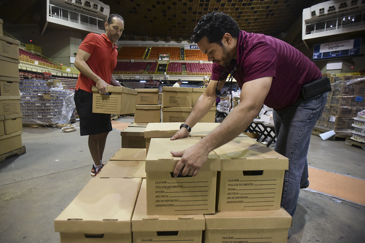 Men move cardboard boxes in a large arena