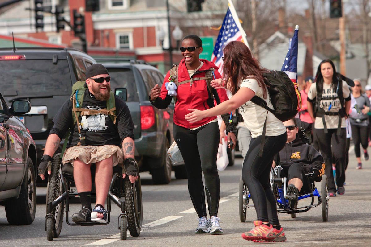 a man in a wheelchair and two walking women converse as they move forward