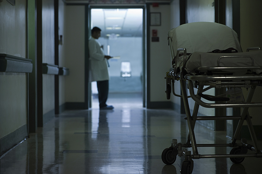 A doctor at the end of a hospital corridor with a hospital bed in the foreground