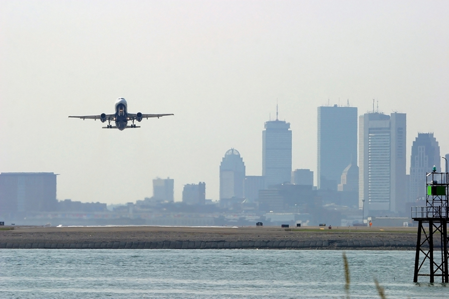A plane leaves Boston Logan Airport with the city skyline in the background