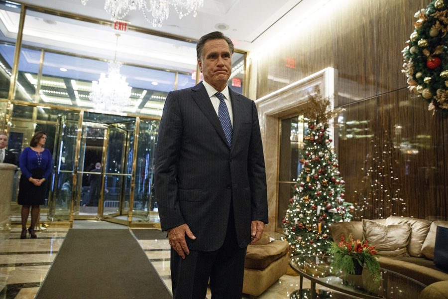 Mitt Romney stands next to a Christmas tree forwning