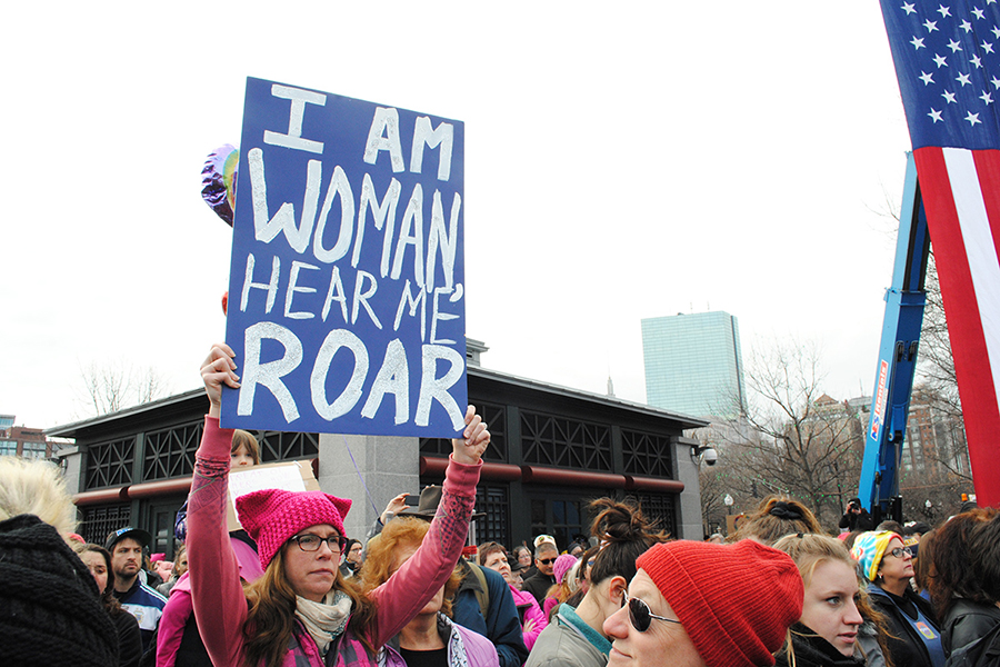 A woman holding a poster that says "I am woman, hear me roar"