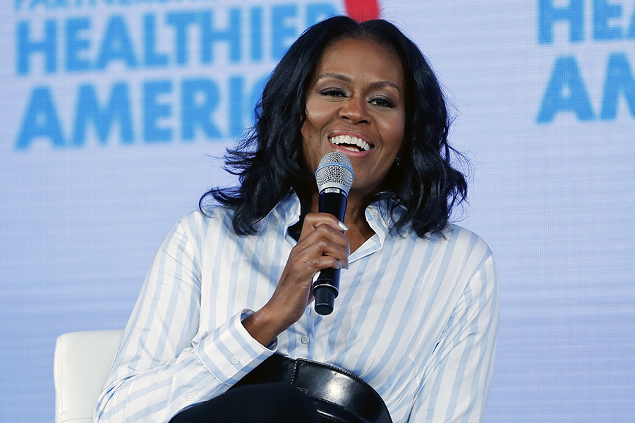 Michelle Obama smiles while holding a microphone