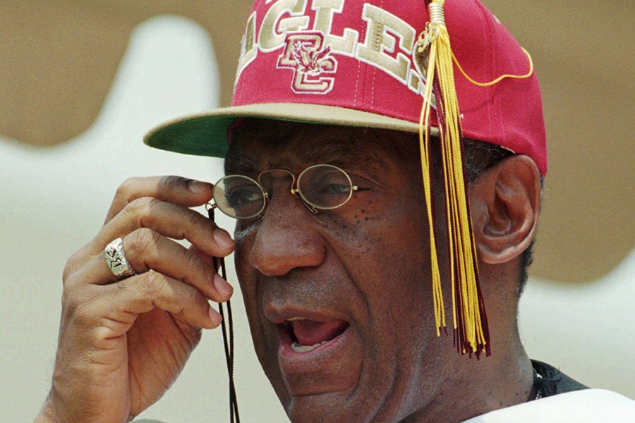 With a Boston College baseball cap replacing his mortarboard, Entertainer Bill Cosby adjusts his reading glasses while delivering his commencement address at Boston College in Chestnut Hill, Mass., Monday May 20, 1996. 