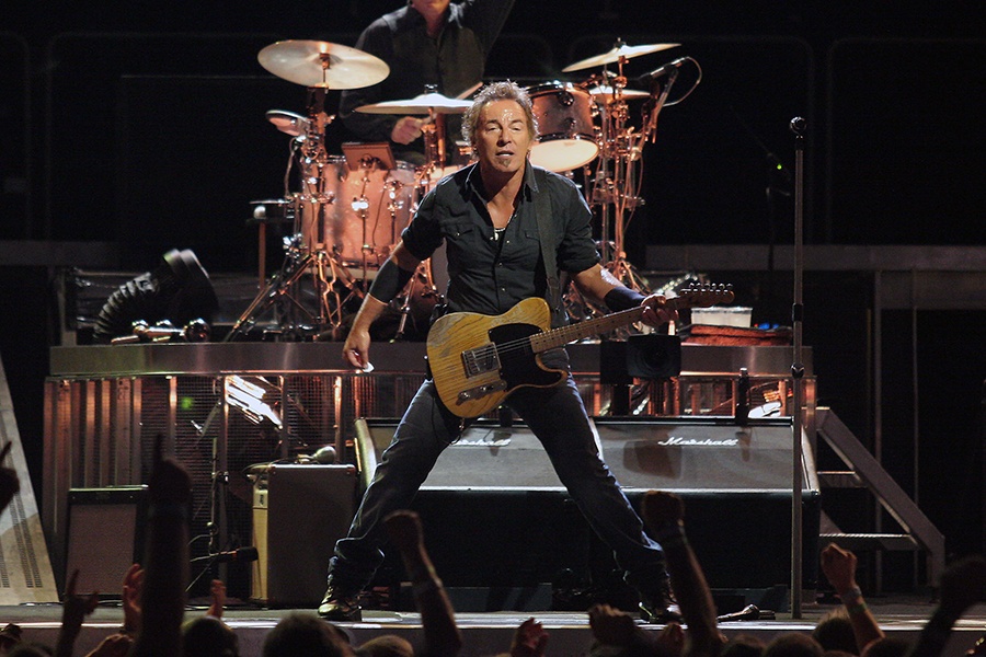 Bruce Springsteen holds a guitar on stage in front of a drummer