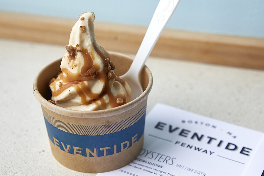 A swirl of caramel-drizzled soft-serve sits in a brown paper cup with Eventide branding.