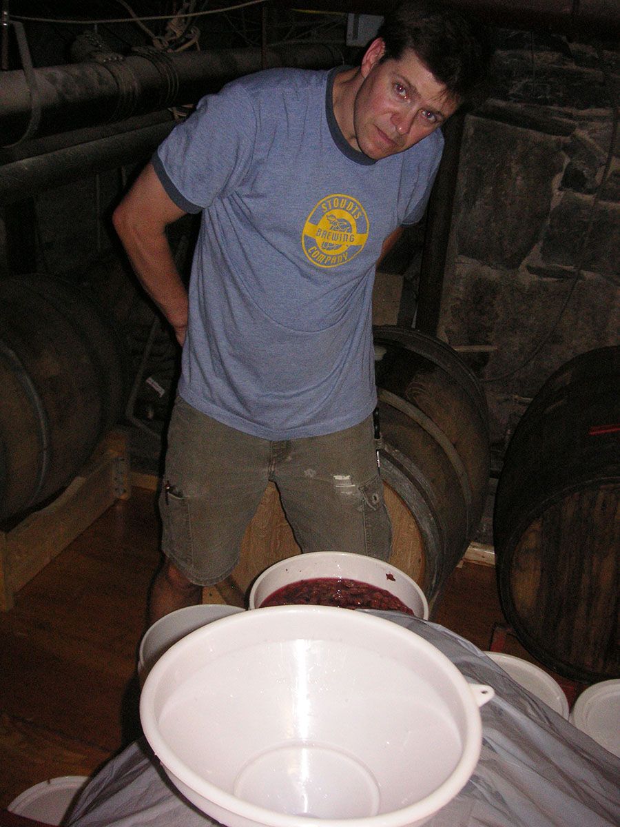 Will Meyers crouches in the barrel cellar at CBC to add fruit to an aging beer