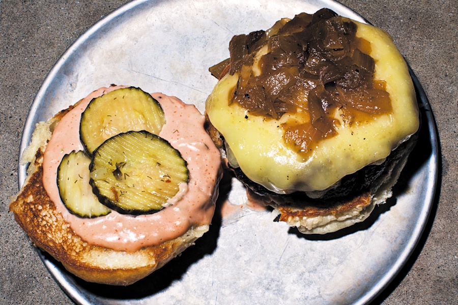 A burger is open to reveal pickles, Russian dressing, cheese, and caramelized onions.