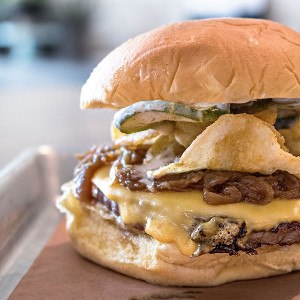 A burger with cheese, fried jalapeno slices, and more toppings.