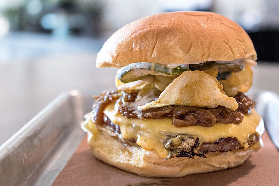 A burger with cheese, fried jalapeno slices, and more toppings.
