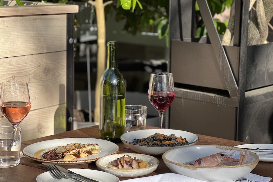 An outdoor restaurant table is covered with upscale dishes that appear Italian, accompanied by a glass of wine.