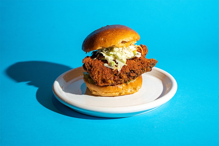 A spicy fried chicken sandwich on a white plate is isolated on a blue background.