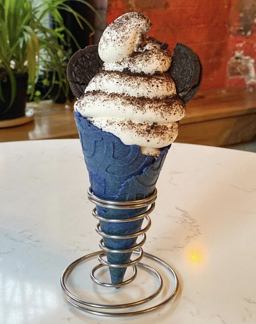 A blue ice cream cone is full of a swirl of vanilla ice cream with a dusting of Oreo crumbs and two big Oreo chunks.