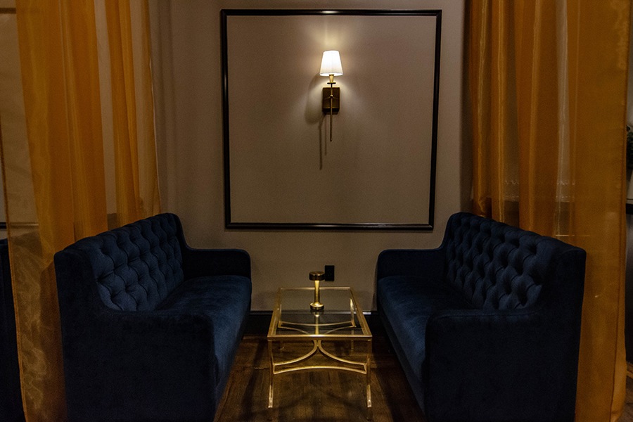 Two velvet blue couches sit on either side of a glass table with gold embellishments in a dimly lit lounge.