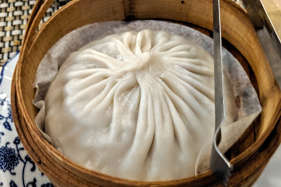 A giant soup dumpling sits in a bamboo steamer basket.