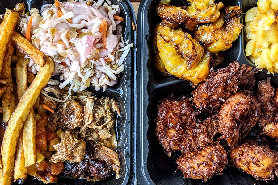 Jamaican food in takeout containers, including jerk chicken and golden brown crispy shrimp.