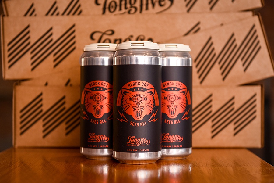 Three beer cans feature red cat-themed art on a black label.