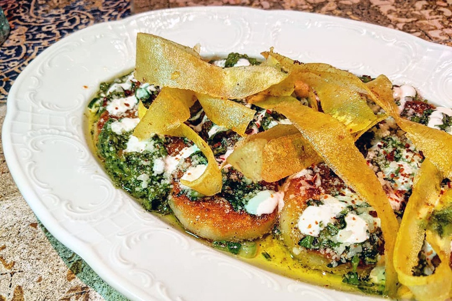 Large fried gnocchi are topped with a green pesto and crispy strips of dough.