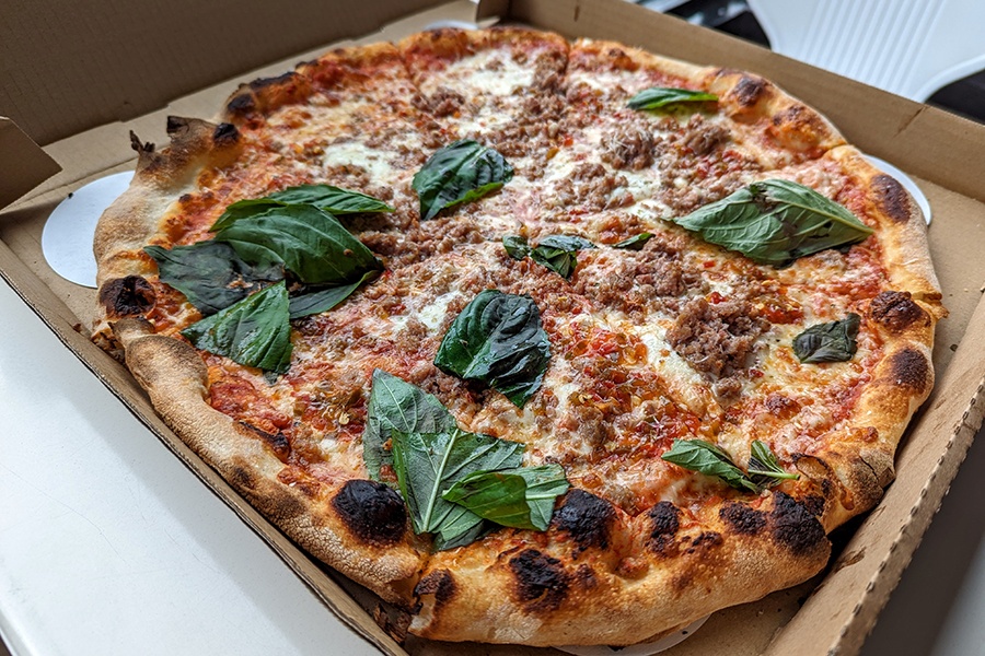 A pizza is topped with crumbled sausage and fresh basil and has a bubbly, charred crust.