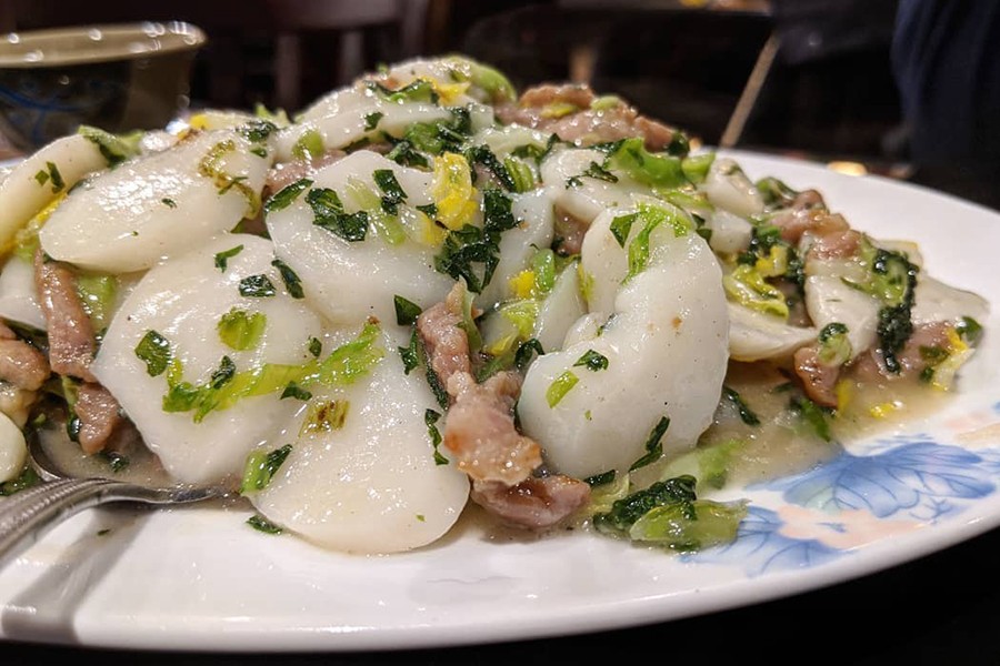 White, oval-shaped rice cakes are stir-fried with finely chopped greens and small pork strips.