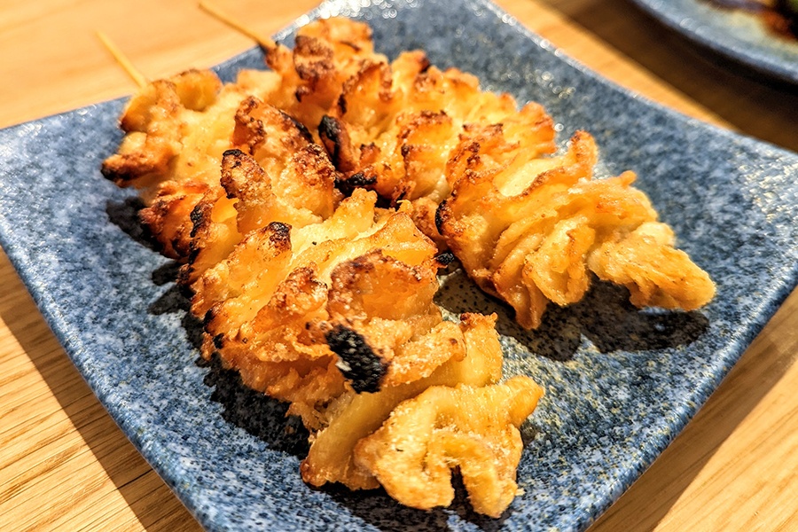 Ribbons of crispy chicken skin are skewered and sit on a decorative plate.