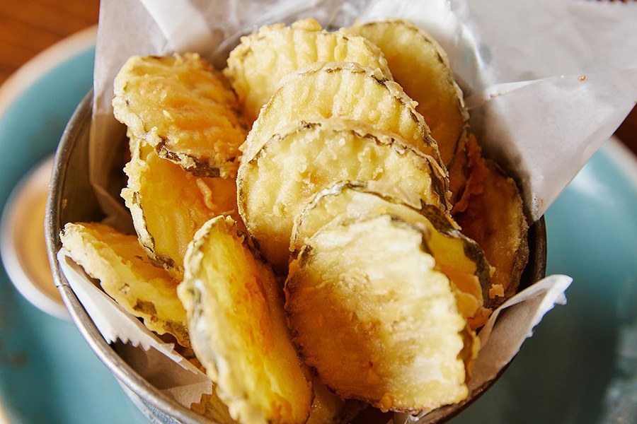 Crispy circles of fried pickles fill a small silver bowl.
