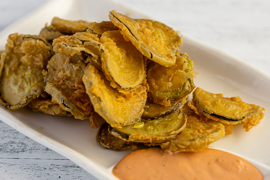 Thin-sliced pickle rounds are breaded and fried golden brown, served with a thick orange dipping sauce.