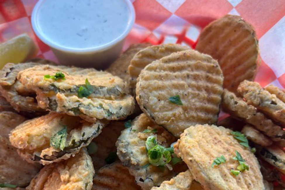Ridged oval fried pickles are golden brown and topped with green scallions, with a side of thick white sauce.