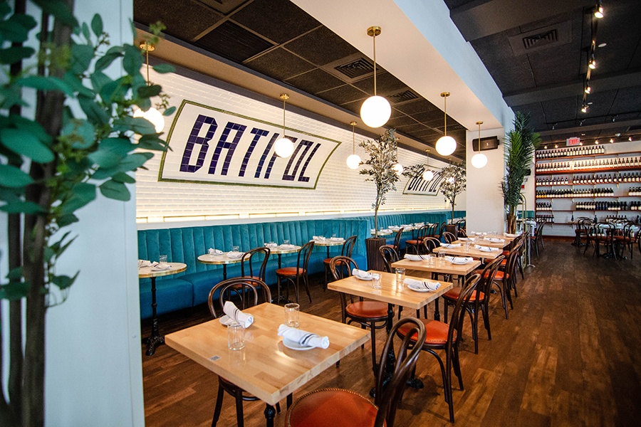 Interior image of a French restaurant with a curved wall covered in white subway tiles and black lettering reading Batefull.  Plush teal banquettes lined the wall.