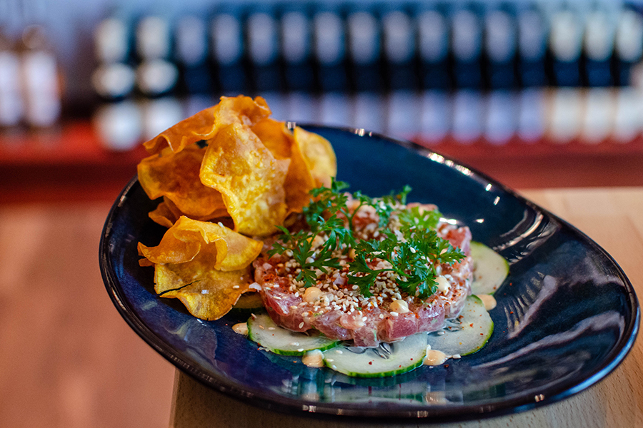 Tuna tartare is served on a bed of thinly sliced cucumbers and garnished with herbs and a side of golden brown potato chips.
