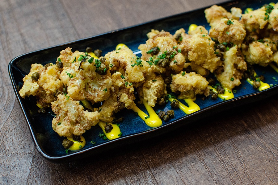 Crispy fried cauliflower is laid out on a rectangular plate on a zig-zag of thick yellow sauce.