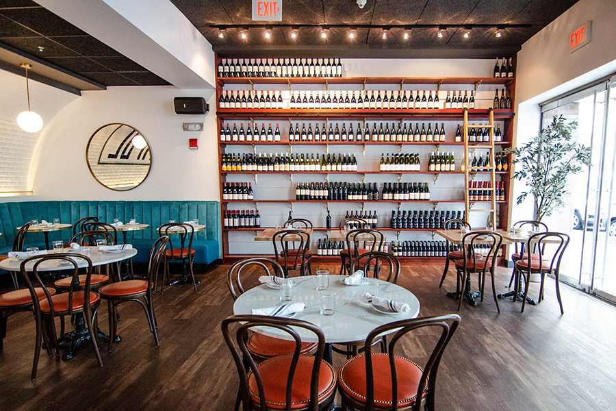 Interior view of a brightly lit restaurant featuring shelves of wine with a ladder to get to the highest shelf.