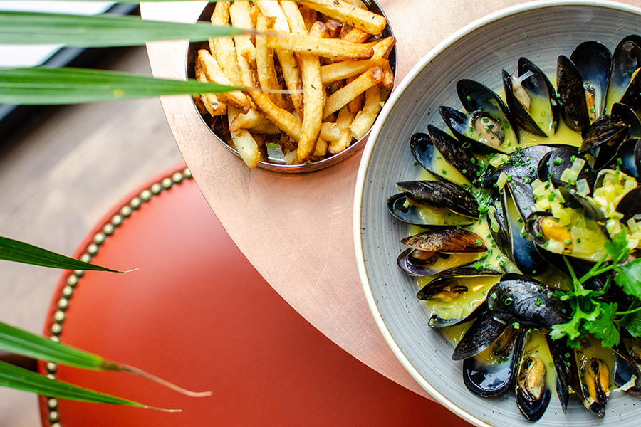 Overhead view of steamed mussels in a yellow broth with a side of fries.