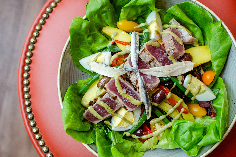 Top view of a French salad with slices of pink tuna, anchovies, and a twist of a creamy green dressing.