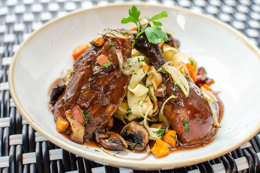 Place the dark brown-coated chicken pieces atop a pile of thick pasta with mushrooms, carrots, and garnished parsley.