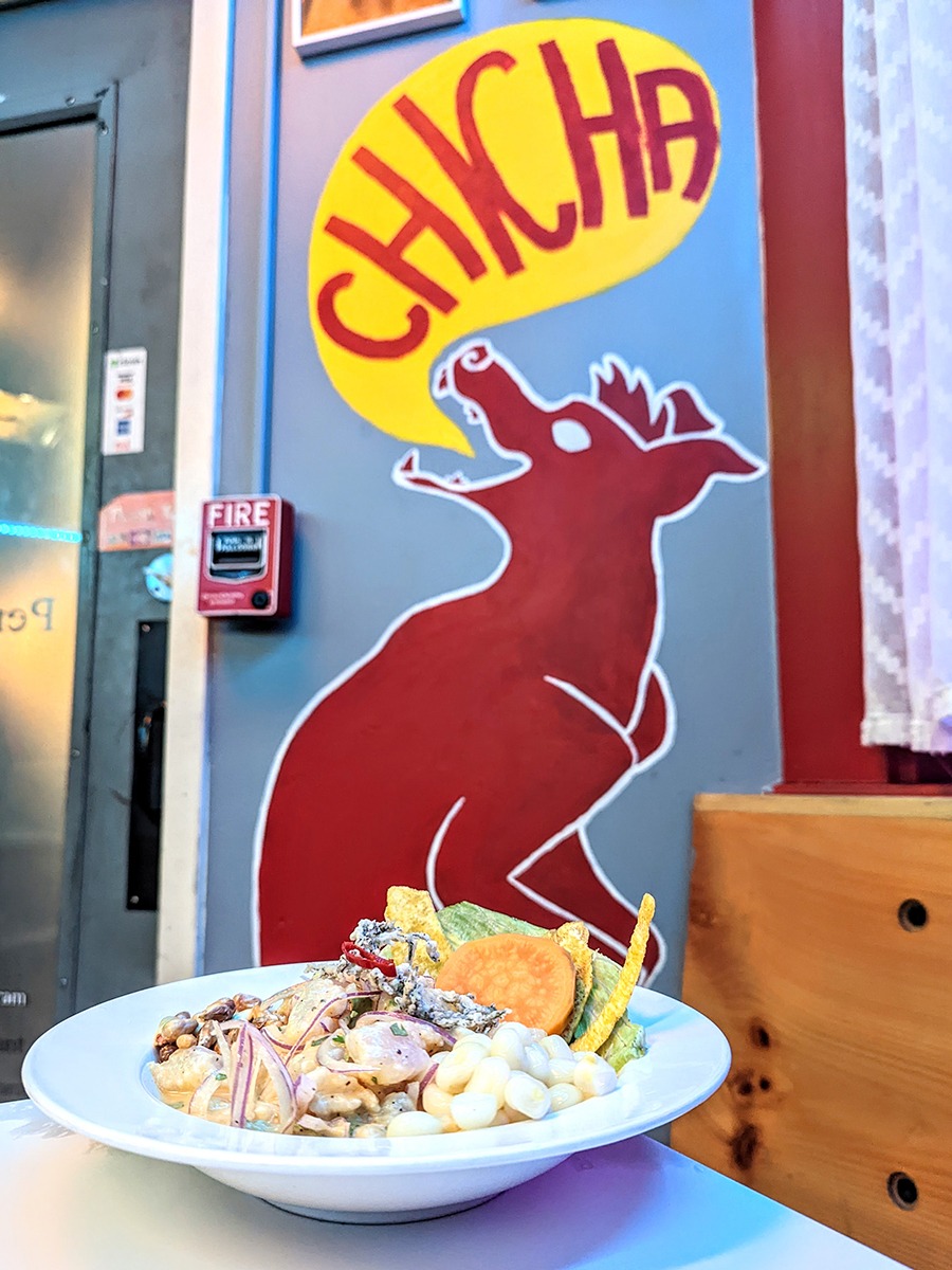 A bowl of ceviche sits in front of a wall adorned with a large red dog saying 