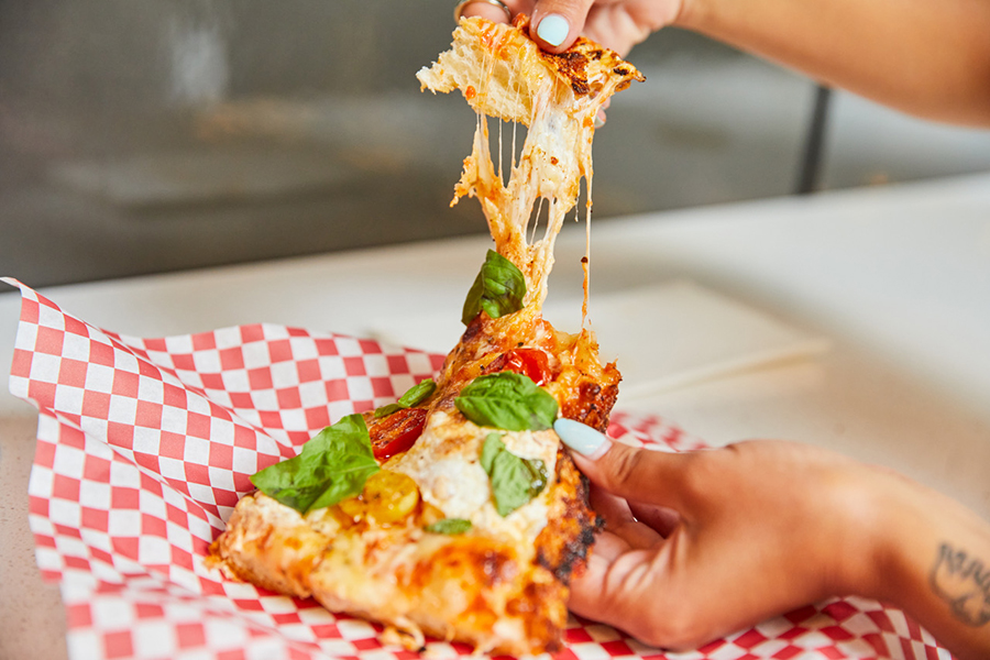 A hand pulls apart a slice of thick-crust pizza topped with basil and stretchy cheese.