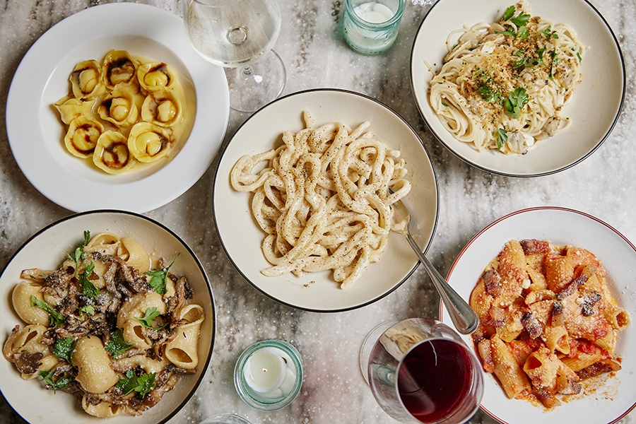 Overhead view of white marble table covered with five different pasta dishes.