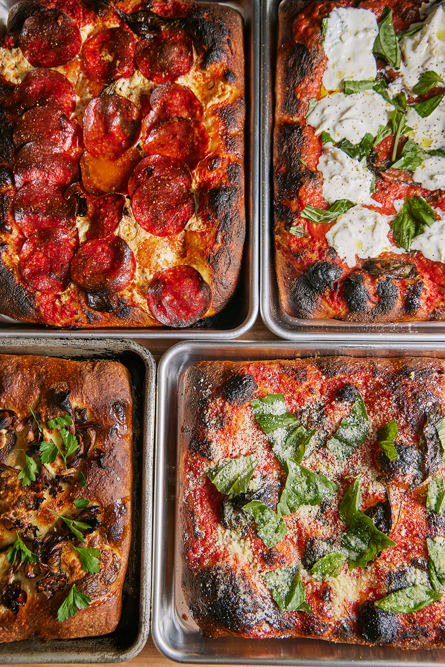 Overhead view of four thick-crust rectangular pizzas in silver trays.