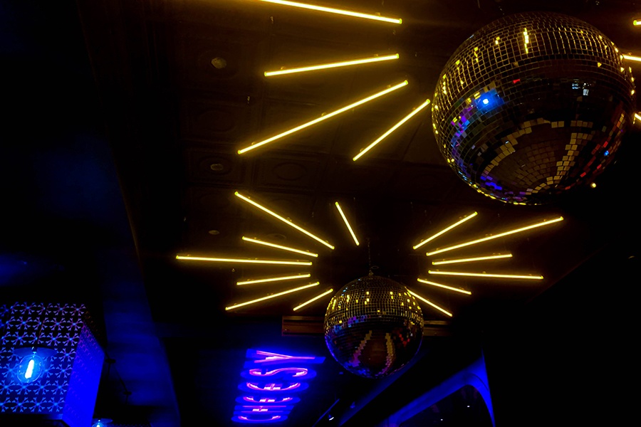 Disco balls and neon lettering reading "cheesy" decorate a ceiling in a restaurant.