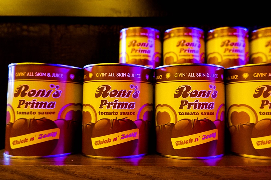 Red and yellow cans of tomato sauce have labels reading "Roni's Prima: Thick 'n' Zesty."