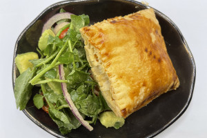 A square-shaped golden-brown Haitian patty is accompanied by a small salad.