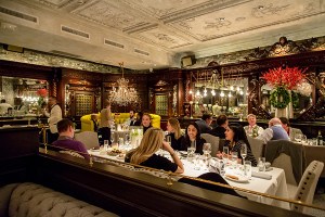 People dine in a glamorous restaurant with servers in white dinner jackets. Subtle Christmas decorations are hanging up.