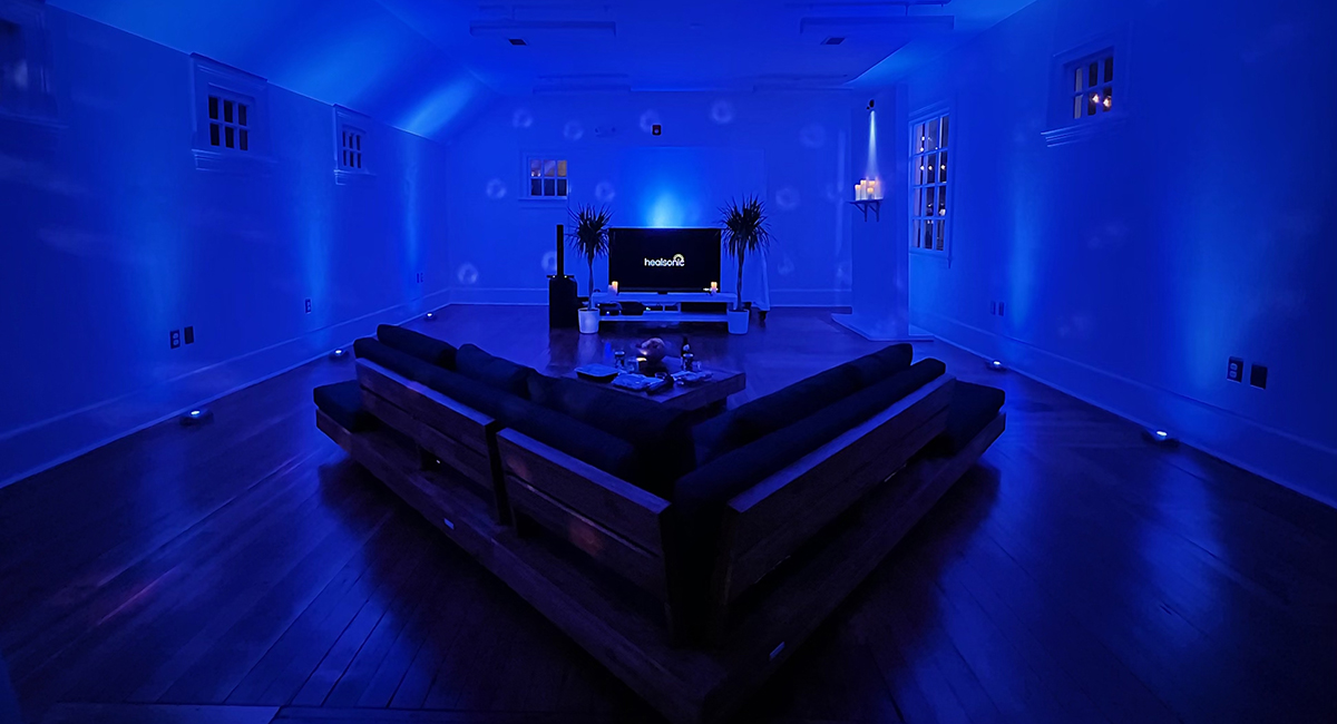 A dim room illuminated with blue lighting features lounge seating and a karaoke machine.