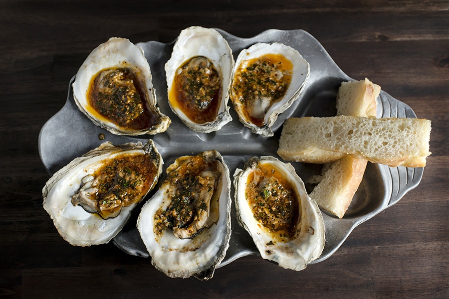 Overhead view of a half dozen oysters with a brownish sauce and a couple pieces of bread on the side.