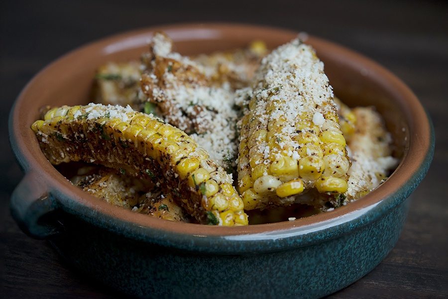 Strips of corn are served in a bowl, topped with crumbled cheese and chili powder.