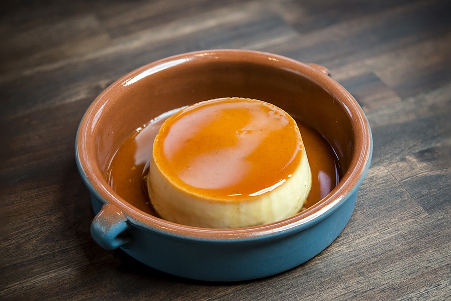 An elegant round of caramel-topped flan sits in a brown and blue bowl.